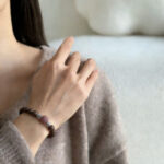 Woman wearing the Butterfly Scent in Spring Moon Bracelet on her wrist, close-up shot showing natural wood beads, the signature pink accent bead, and silver details, in a soft, cozy indoor setting.